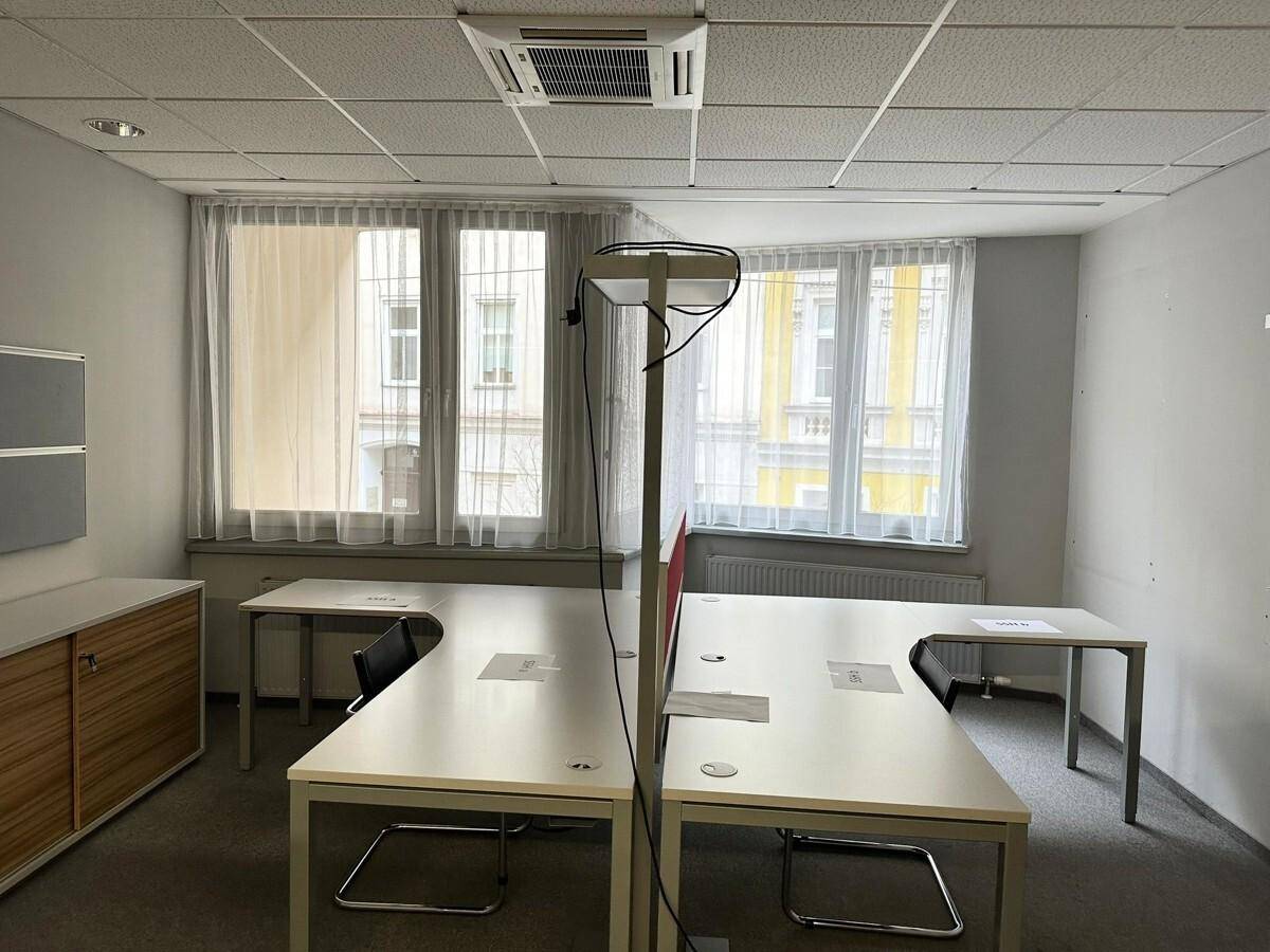 Helles Büro mit mehreren Arbeitsplätzen, Teppichboden und großen Fenstern mit Blick auf die Stadt.