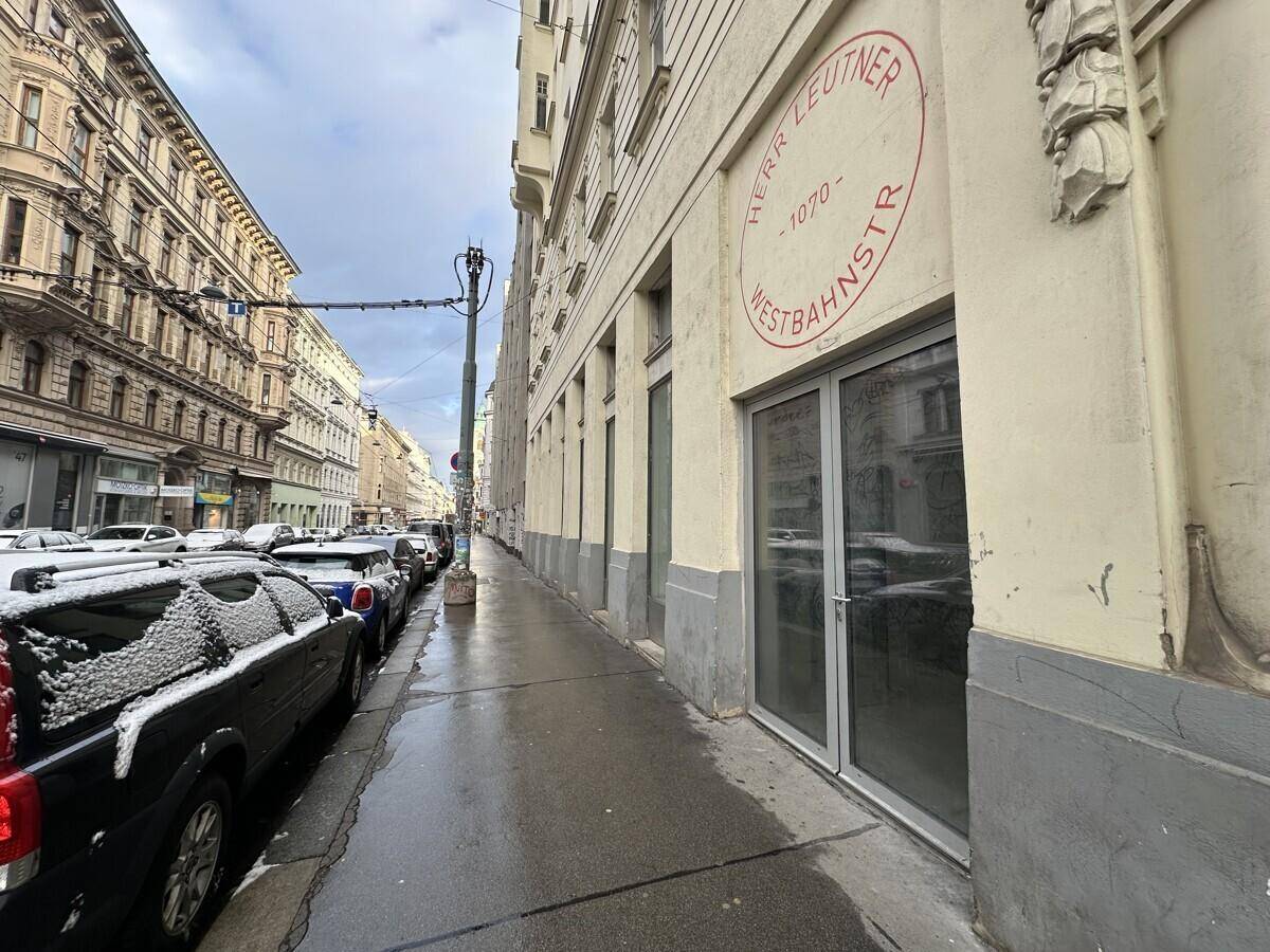 Die lange Fassade eines Altbaus entlang einer städtischen Straße mit parkenden Autos und winterlicher Atmosphäre.
