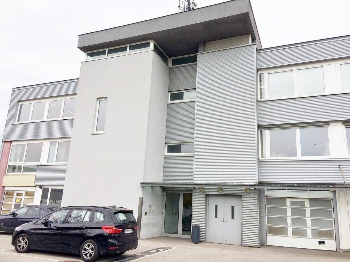 Ansicht des modernen Bürogebäudes mit Eingangsbereich und geparktem Fahrzeug.