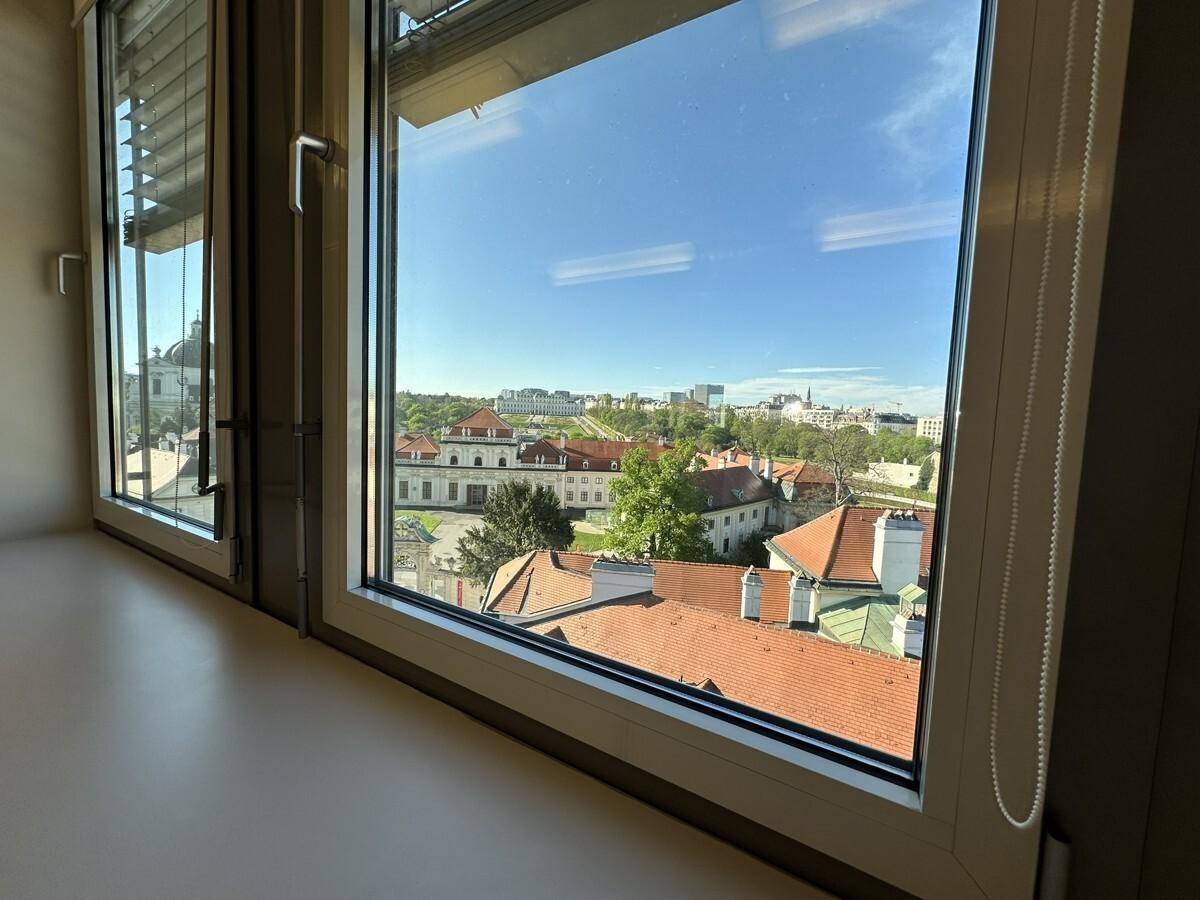Weitblick aus dem Fenster über eine Stadtlandschaft mit historischen Gebäuden und viel Grün unter blauem Himmel.
