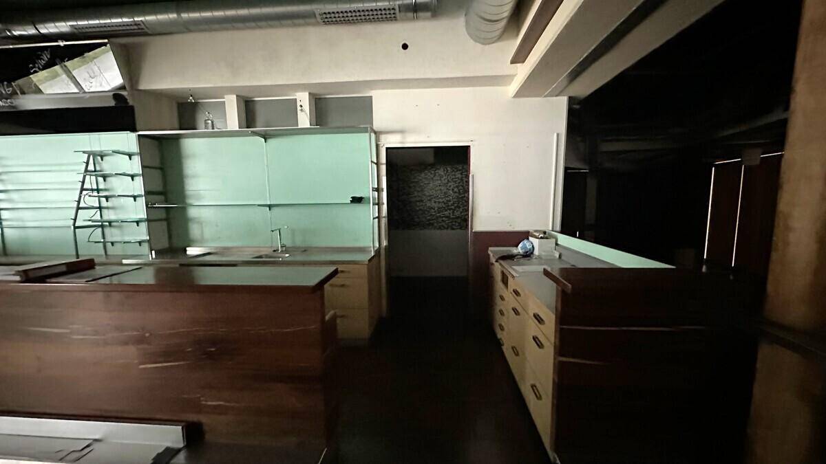 Hinterer Bereich eines Geschäftsraums mit Arbeitsflächen, Regalen und sichtbaren Lüftungsrohren.