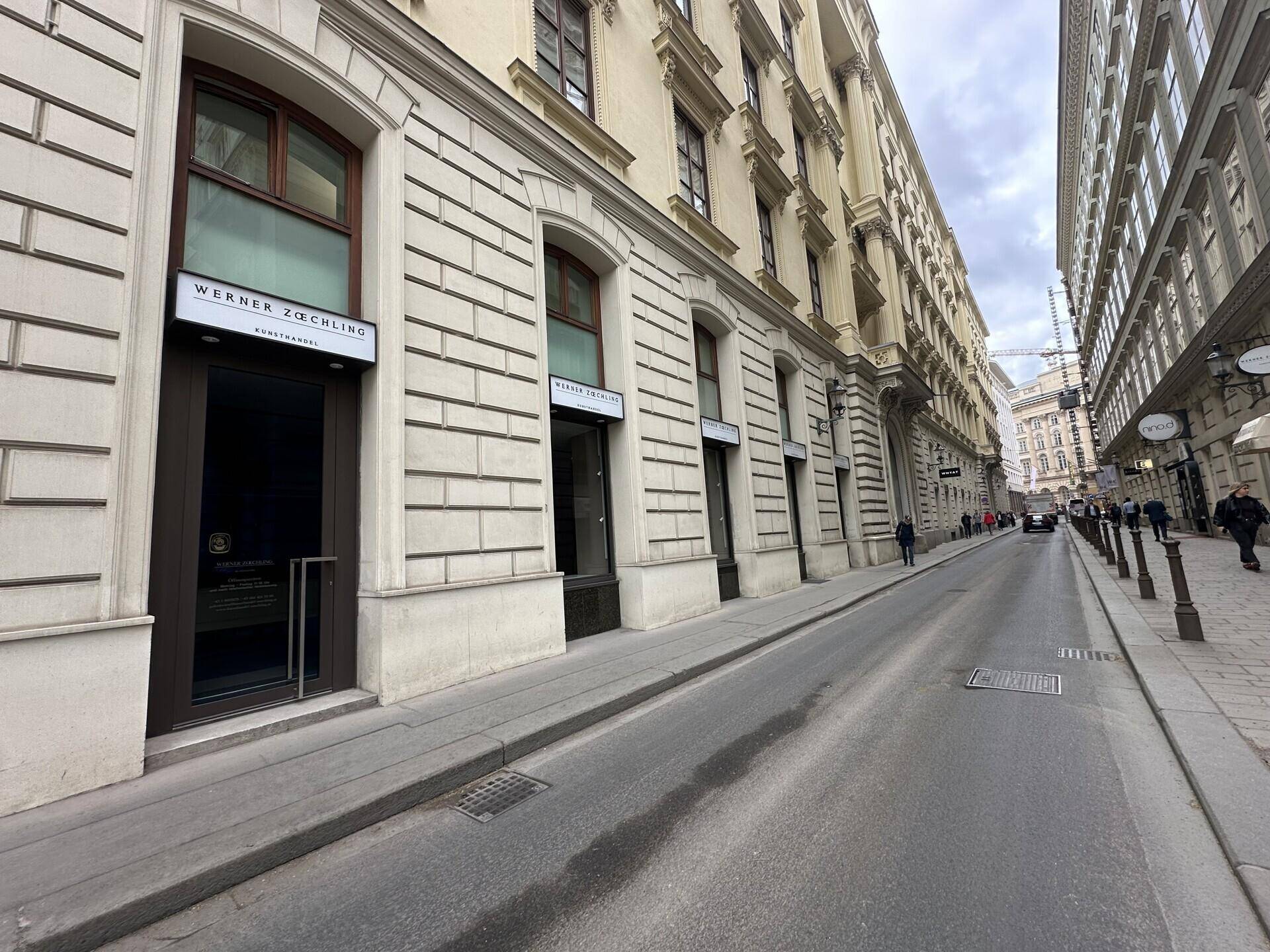 Seitenansicht des historischen Gebäudes mit Schaufenstern und Passanten auf der Straße.