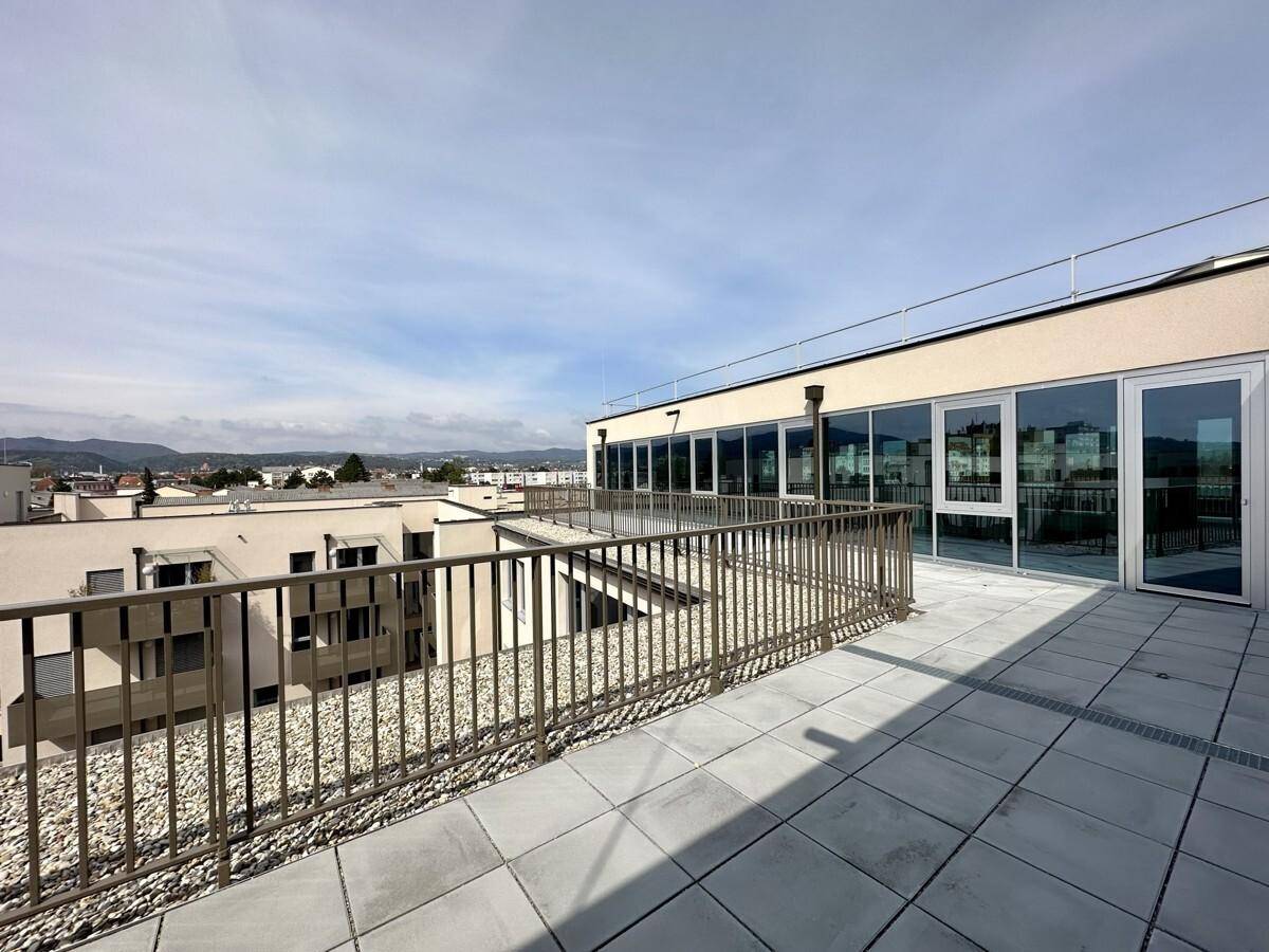 Weitläufige Dachterrasse mit Zugang zum Gebäude und Panoramablick auf die umliegende Landschaft und Stadt.