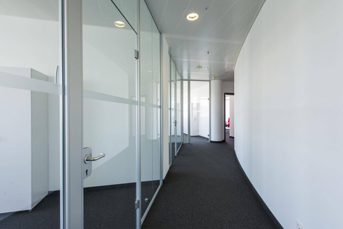 Leeres Büro mit Schreibtischen, roten Stühlen und weitem Blick durch große Fenster.