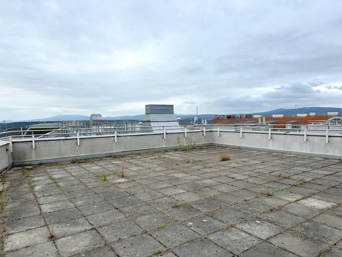 Große Dachterrasse mit Betonplatten und weitem Blick über die Stadt und die umliegenden Berge.