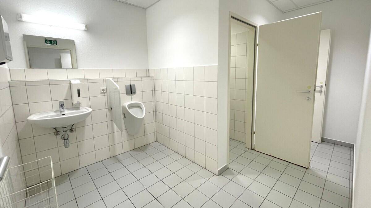Sauberer öffentlicher Waschraum mit weißen Fliesen, Waschbecken und Urinal.