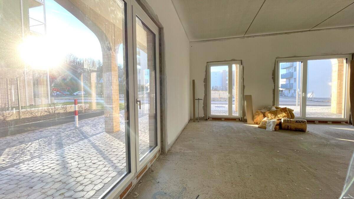 Blick aus dem Rohbau auf den gepflasterten Außenbereich und die Straße, mit starker Sonneneinstrahlung.