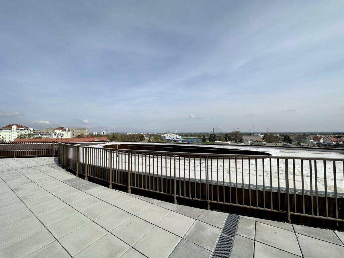 Geräumige Dachterrasse mit Fliesenboden und Metallgeländer, die einen weiten Blick über die Stadt ermöglicht.