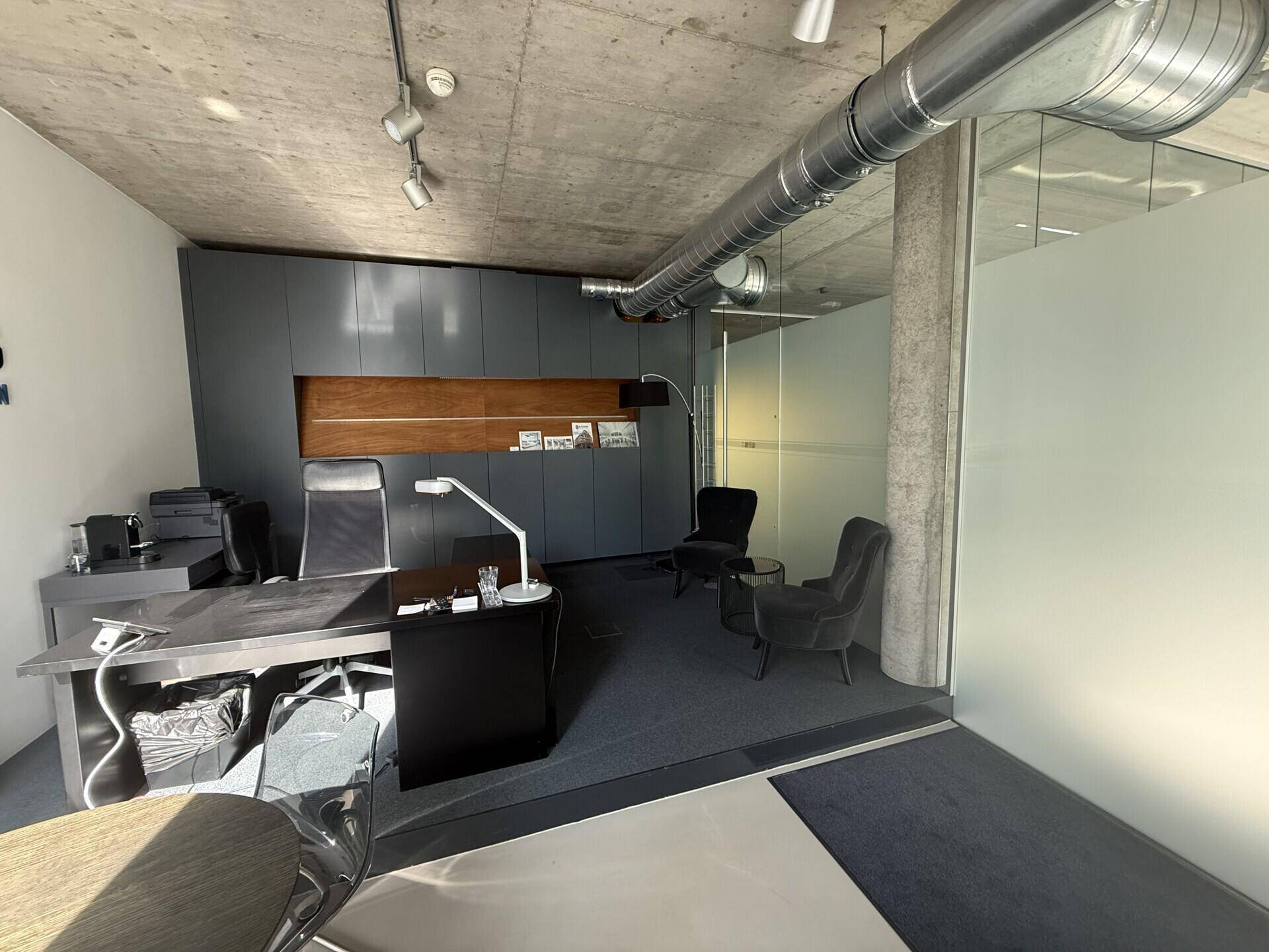 Modernes Büro mit Teppichboden, Sichtbetondecke und freiliegenden Lüftungsrohren im Industriedesign.