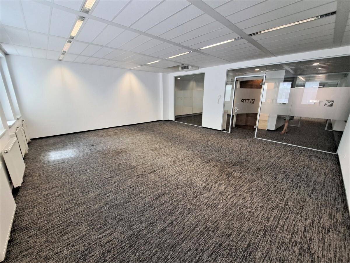 Leeres Büro mit Teppichboden, Glaswänden für separate Bereiche und viel Tageslicht.