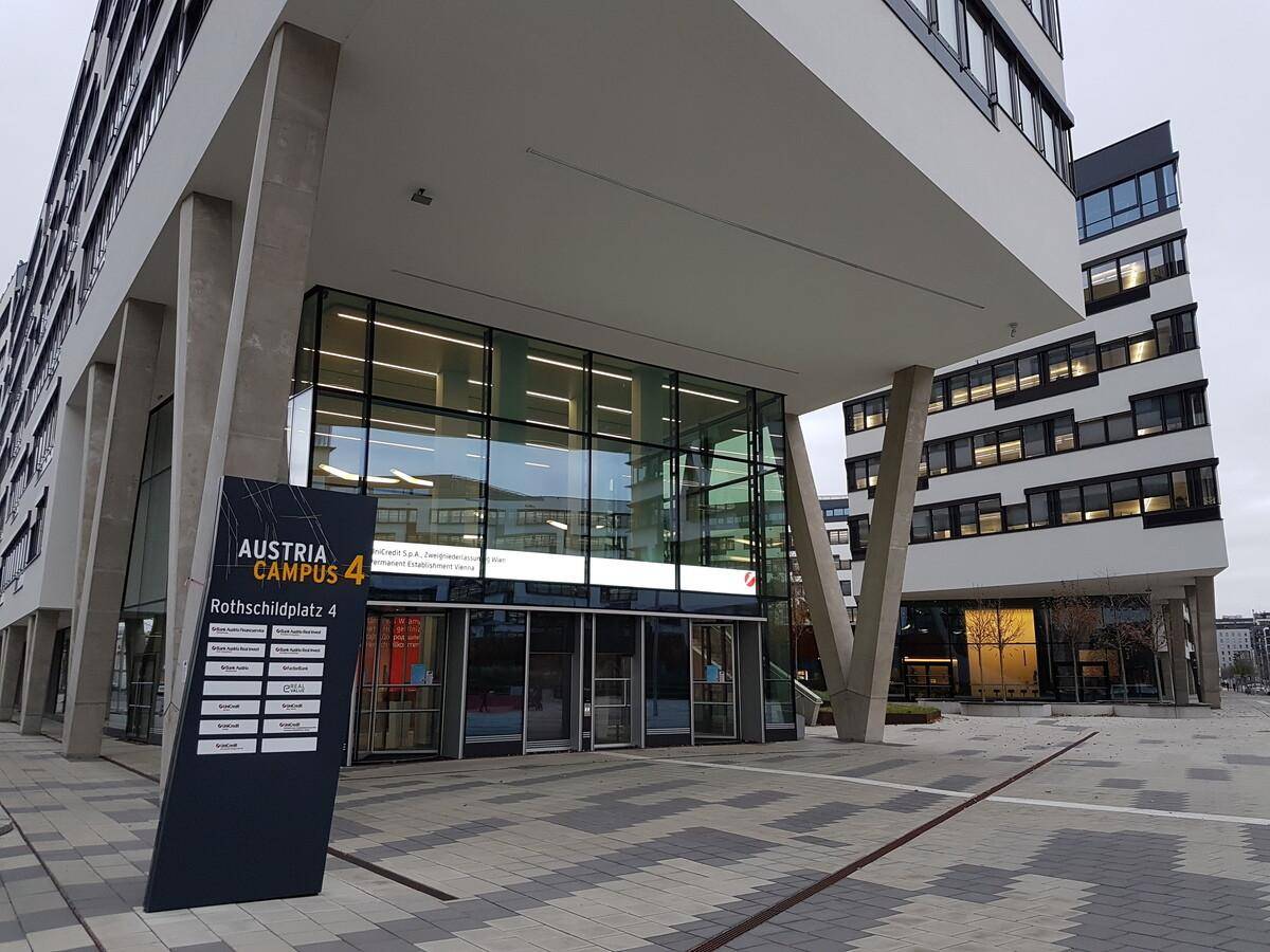 Eingangsbereich eines modernen Bürogebäudes mit Glasfassade und Informationsstele.