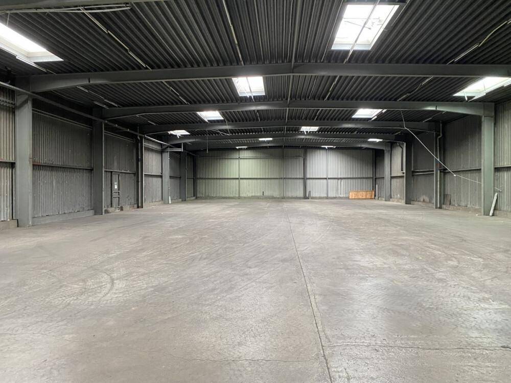 Weitläufige, leere Lagerhalle mit Betonboden und Oberlichtern für natürliche Beleuchtung.