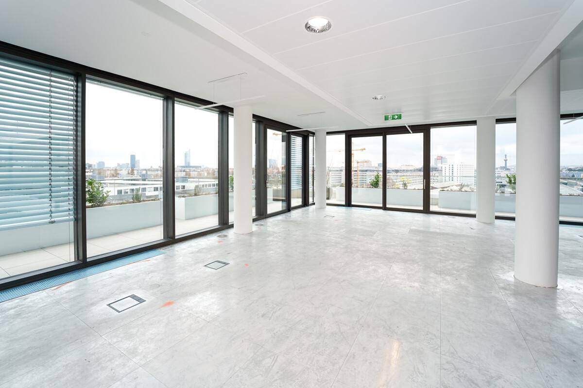 Heller Büroraum mit großen Fenstern, Jalousien und Zugang zu einer Terrasse mit weitem Stadtblick.