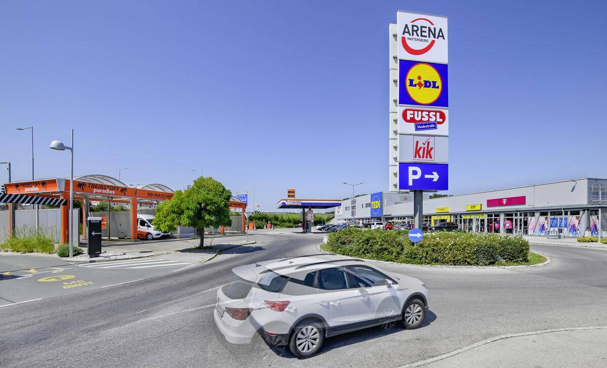 Weitläufiges Gewerbegebiet mit verschiedenen Geschäften, Tankstelle und Waschanlage unter blauem Himmel.