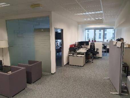 Moderner Bürobereich mit Glaswänden, flexiblen Trennwänden und mehreren Arbeitsplätzen mit Teppichboden.