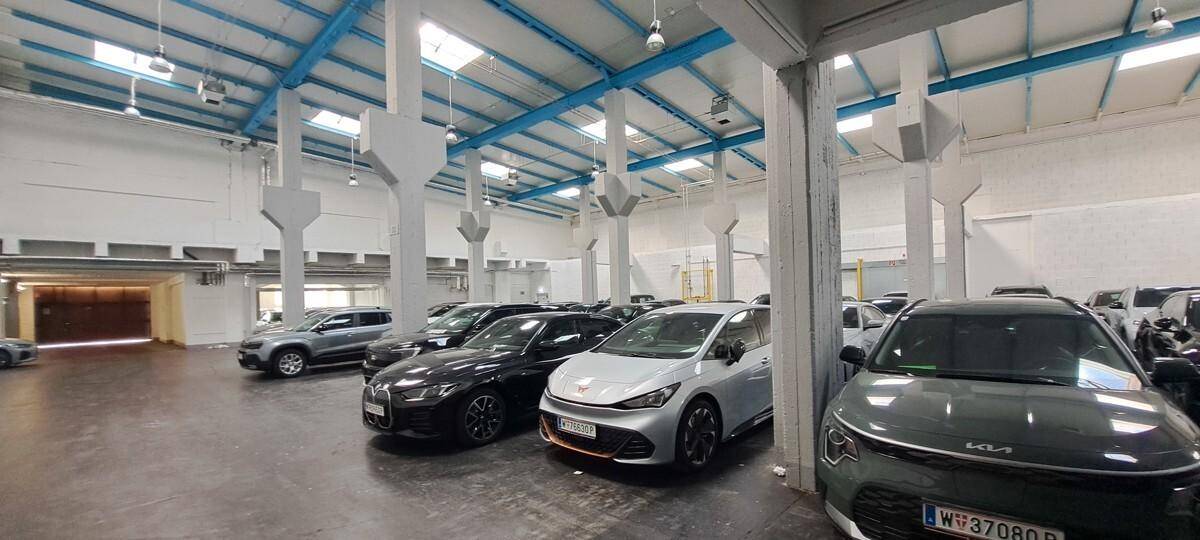 Große, helle Halle mit zahlreichen geparkten Autos, hohen Decken und sichtbaren Stahlträgern.