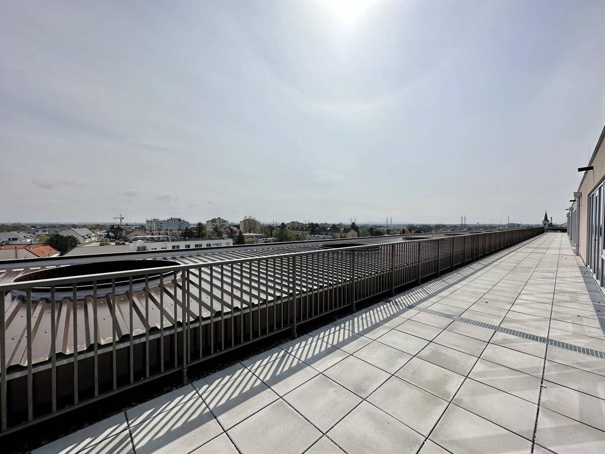 Lange Dachterrasse mit Fliesenboden und Metallgeländer, ideal für Entspannung im Freien mit Weitblick.
