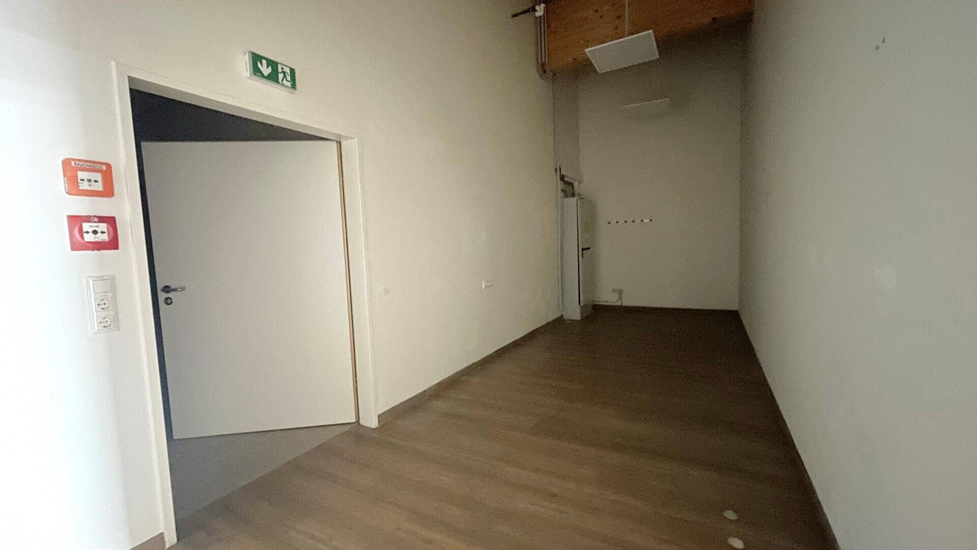 Kleiner Nebenraum mit Holzbalkendecke, hellem Boden und einer weißen Tür, ausgestattet mit Brandschutzmeldern.