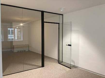 Moderner Büroraum mit Teppichboden, weißen Wänden und einer eleganten Glaswand als Raumteiler.