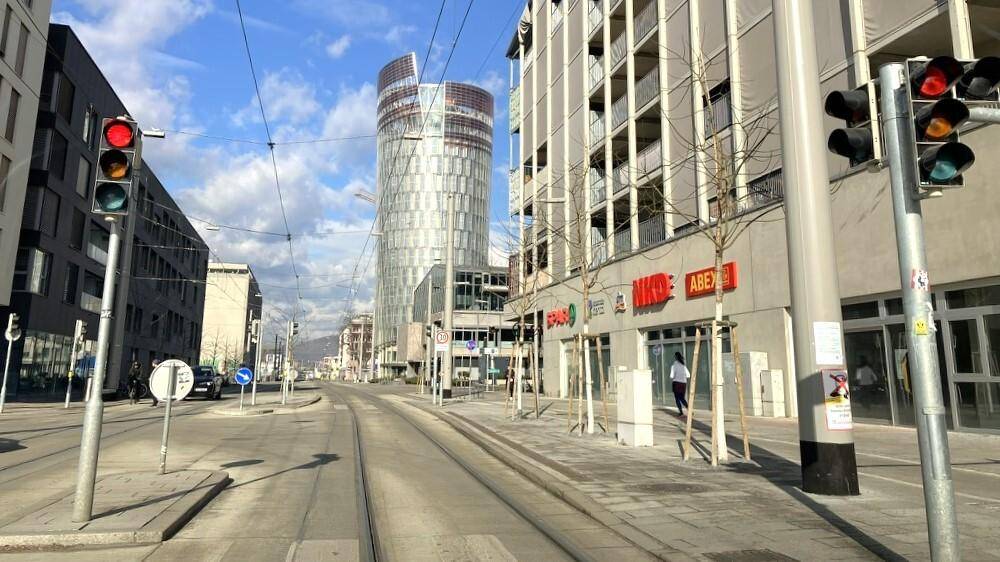 Urbane Straßenszene mit modernen Gebäuden, Straßenbahnschienen und Ampeln unter blauem Himmel.