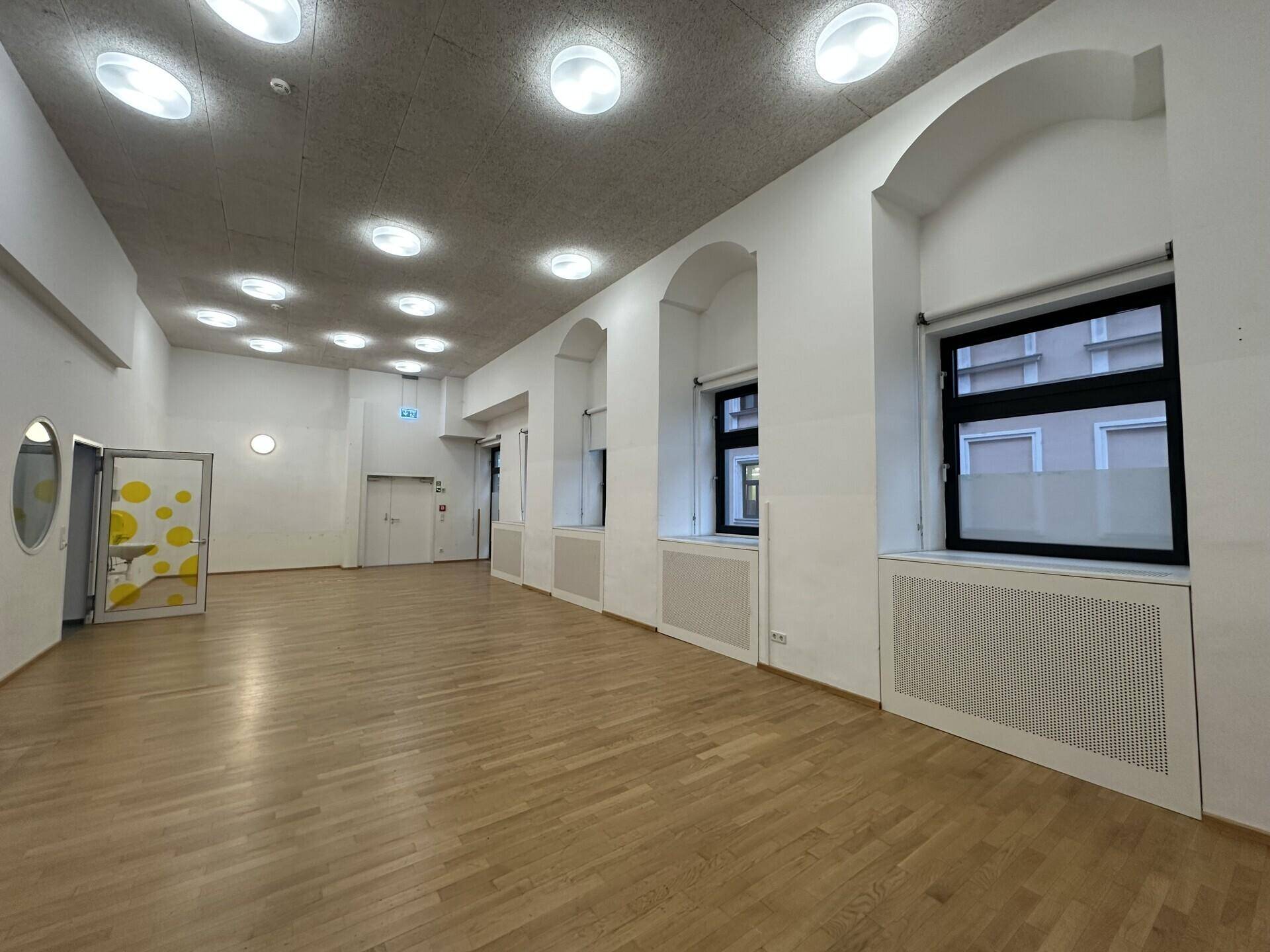 Großer, heller Raum mit Holzboden und vielen Deckenleuchten, ideal für Büros oder Veranstaltungen.