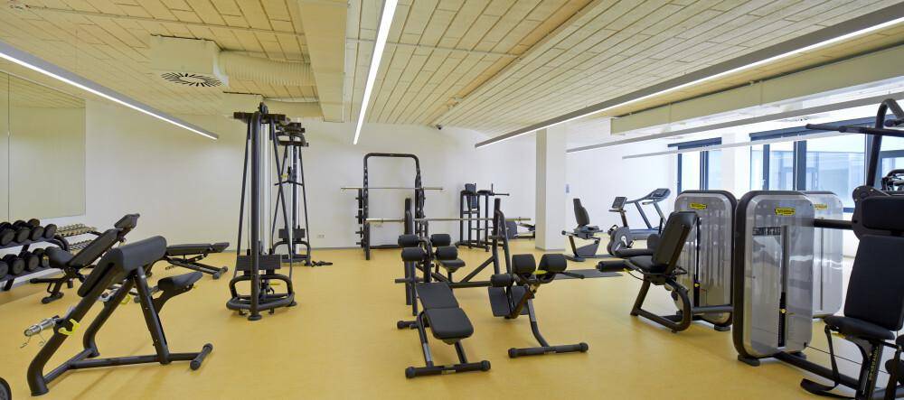 Gut ausgestatteter Fitnessraum mit verschiedenen Trainingsgeräten und gelbem Boden für sportliche Aktivitäten.