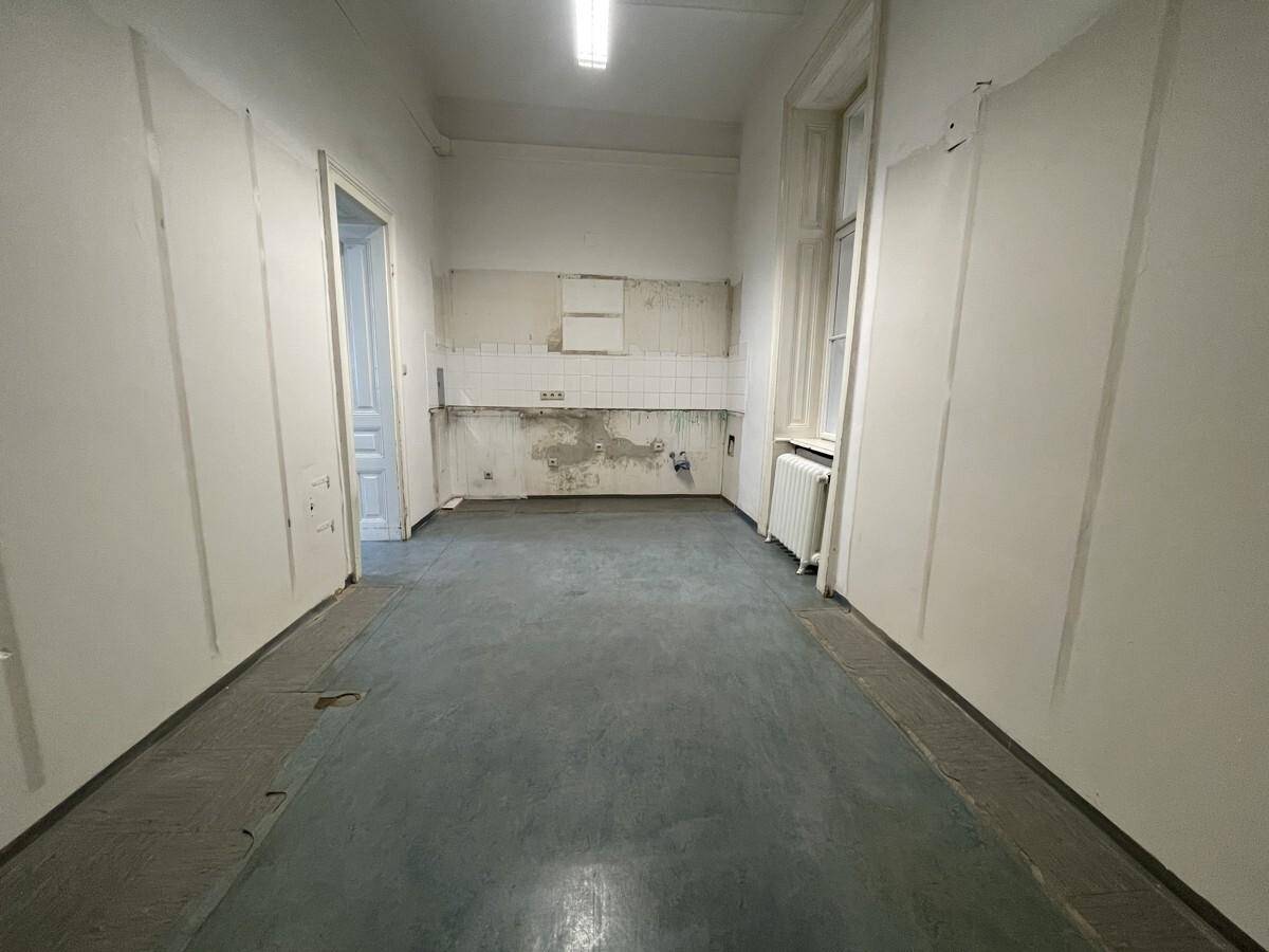Einfache Küche mit Fliesenrückwand und Spuren einer ehemaligen Küchenzeile, renovierungsbedürftig.