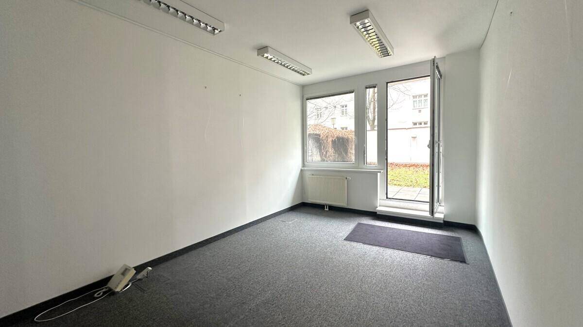 Leerer Büroraum mit Teppichboden und einer Tür, die direkten Zugang zu einem Außenbereich bietet.