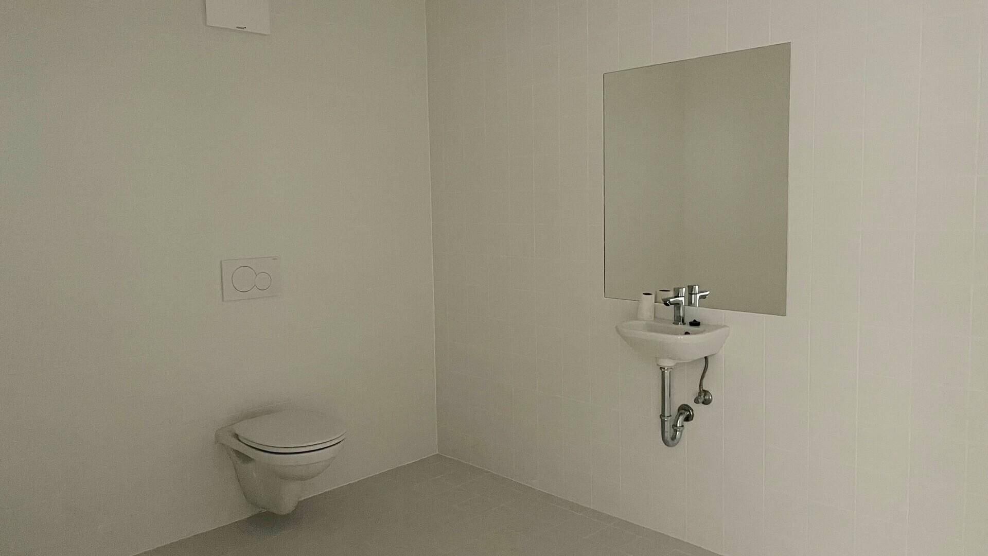 Kleines, fertiggestelltes Gäste-WC mit wandhängender Toilette, Waschbecken, Spiegel und weißen Fliesen.