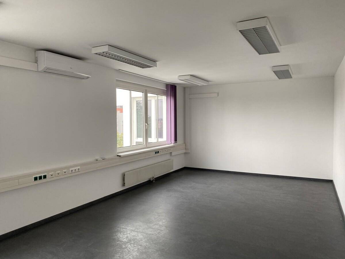 Geräumiger Büroraum mit dunklem Boden, Klimaanlage und Fenster für natürliche Belichtung.