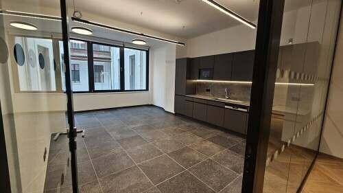 Moderner Bürobereich mit integrierter Küchenzeile, Fliesenboden und großen Fenstern für viel Tageslicht.
