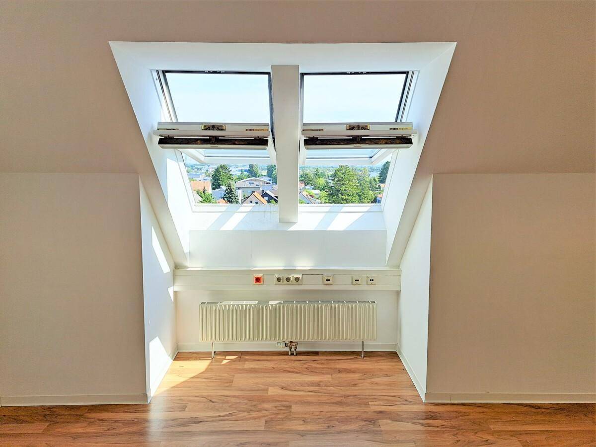 Zwei große Dachfenster in einem Raum mit Schrägen, die einen weiten Blick nach draußen ermöglichen.