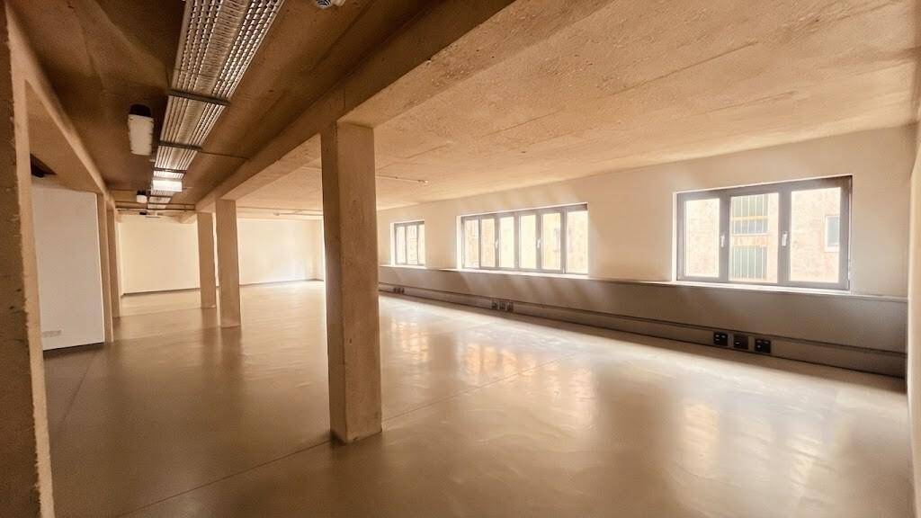 Weitläufiger Bürobereich mit Betonstützen und einer Reihe von Fenstern, die den Raum mit natürlichem Licht füllen.