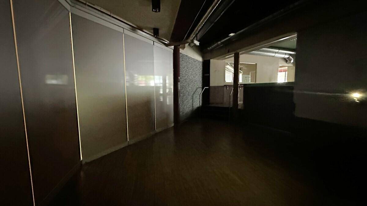 Dunkler Geschäftsraum mit Holzboden, reflektierenden Wandpaneelen und sichtbaren Lüftungsrohren.