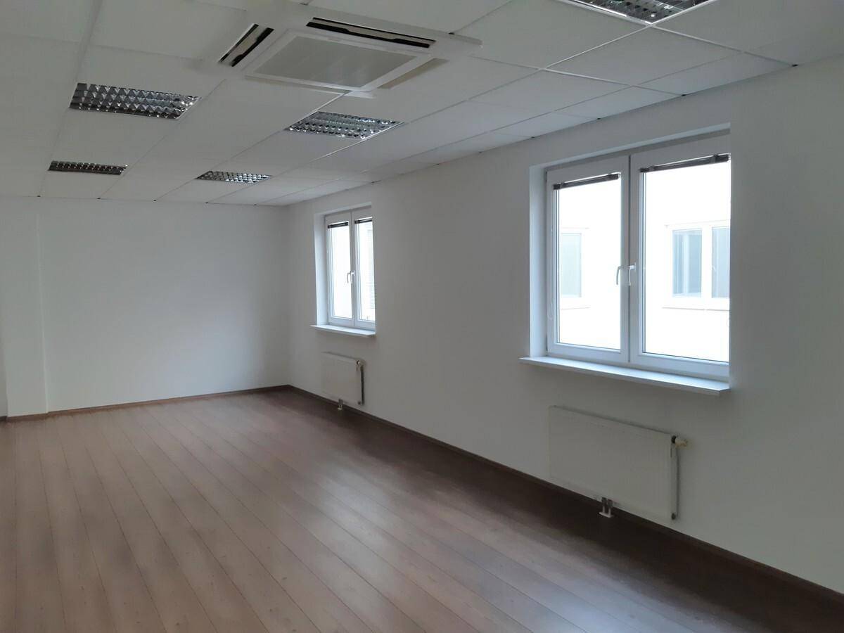 Heller Büroraum mit zwei Fenstern, weiß gestrichenen Wänden und Holzoptik-Laminatboden.