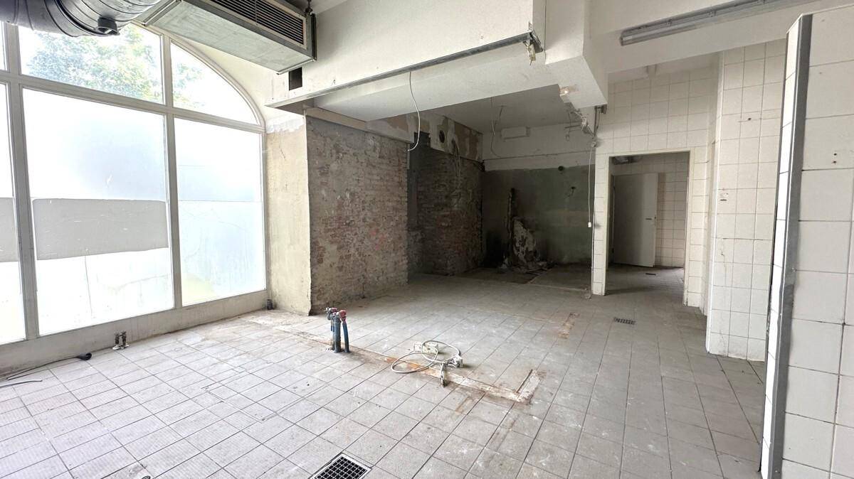 Leerstehende Gewerbeküche mit Fliesenboden, freiliegenden Ziegelwänden und großen Bogenfenstern.