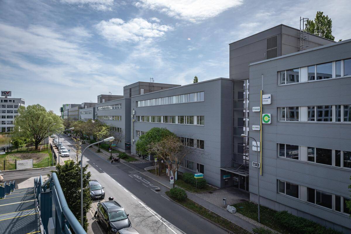 Überblick über einen modernen Bürokomplex mit grauen Fassaden, einer Straße und geparkten Autos unter bewölktem Himmel.