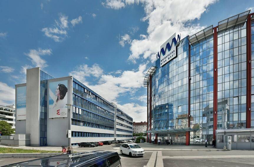 Weitwinkelaufnahme eines modernen Bürokomplexes mit Glasfassaden und umliegenden Straßen unter blauem Himmel.