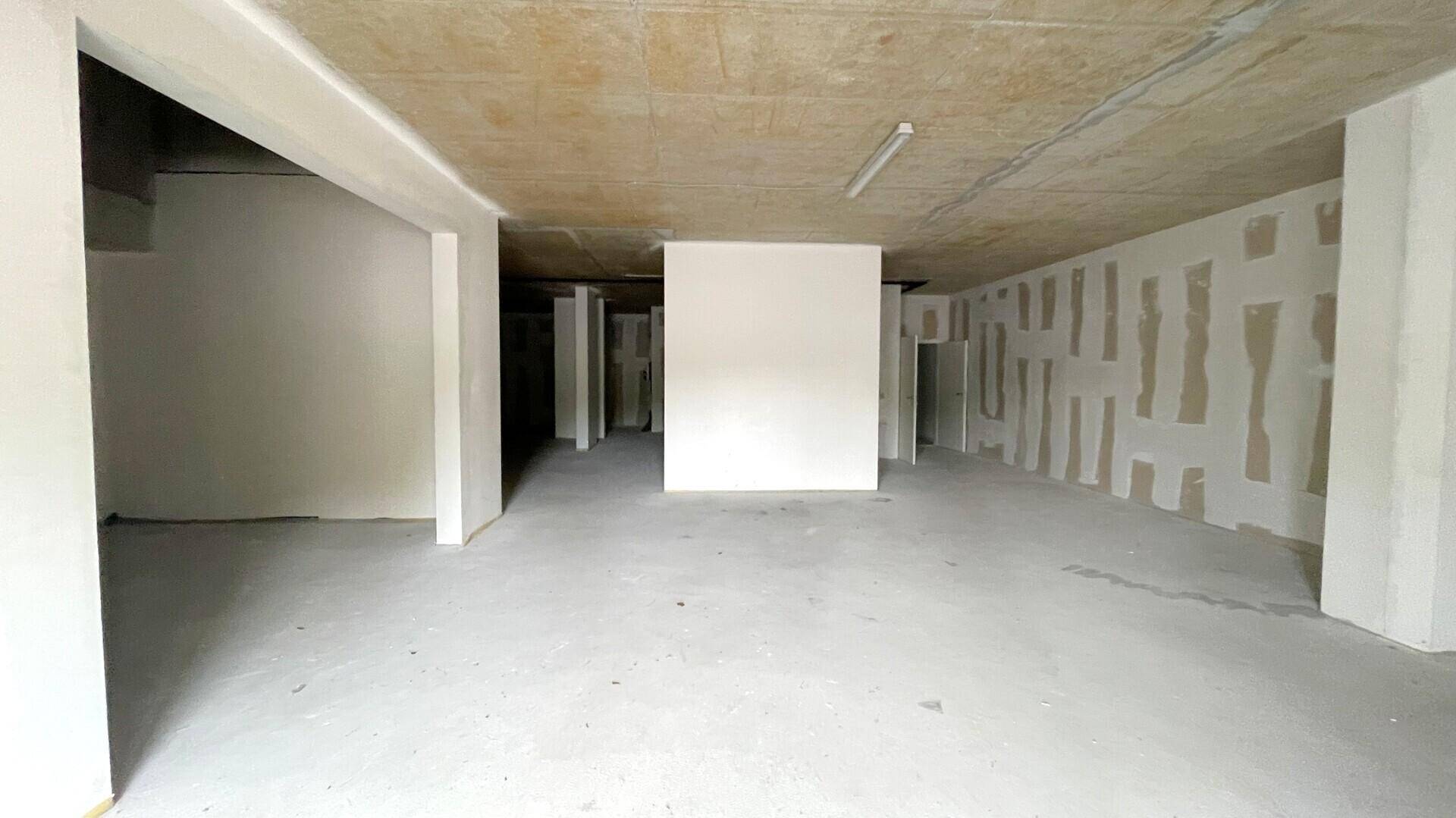 Großer, unfertiger Innenraum mit Betonboden und -decke, teilweise verputzten Wänden und einfacher Beleuchtung.