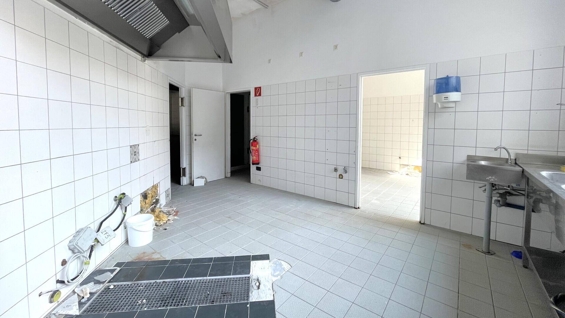 Gewerbeküche mit gefliesten Wänden, Edelstahlarbeitsflächen und sichtbaren Installationsarbeiten.