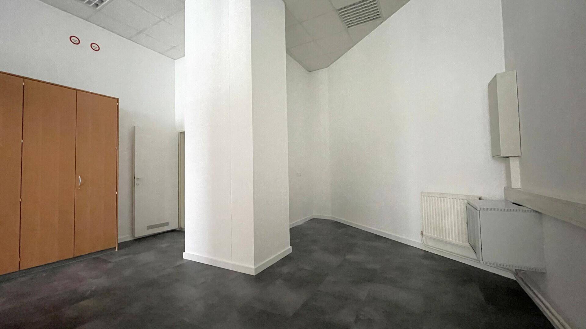 Heller Büroraum mit einem zentralen Pfeiler, dunklem Boden und einem Heizkörper an der weißen Wand.