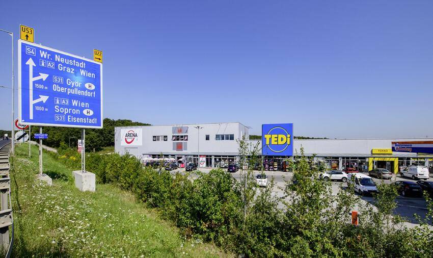 Einkaufszentrum mit TEDI-Schild und einer großen Straßentafel, die verschiedene Fahrtrichtungen anzeigt.