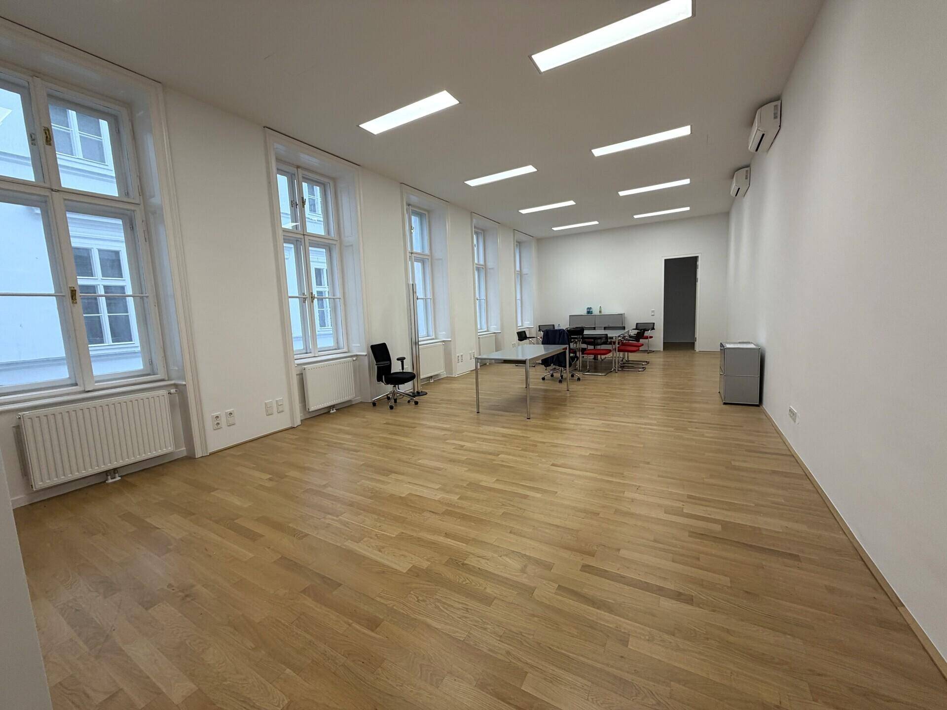 Großes, helles Büro mit Holzfußboden, vielen Fenstern und Klimaanlage an der Wand.