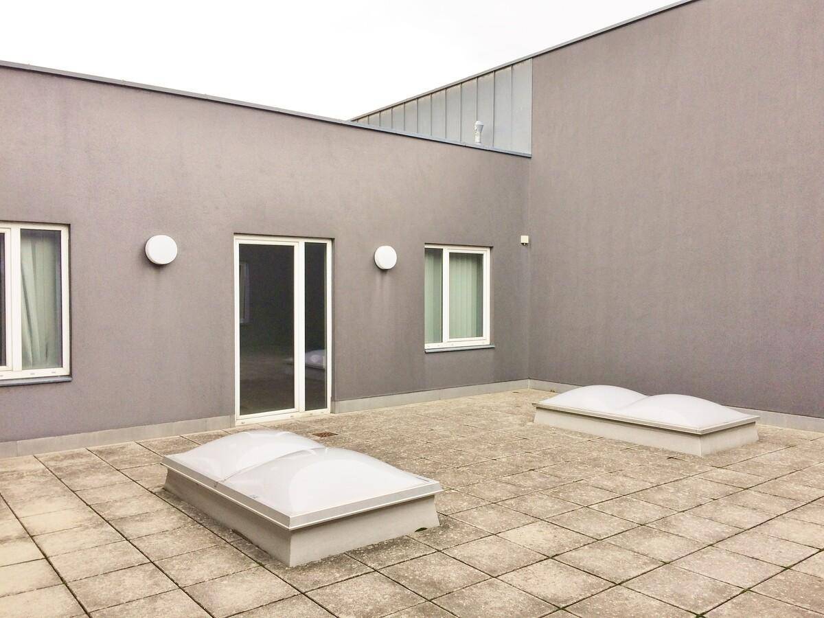 Ruhige Dachterrasse mit grauen Fliesen, Oberlichtern und einer Tür, die ins Gebäude führt.