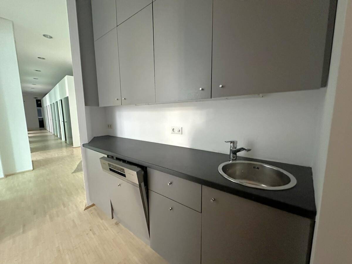 Moderne Küchenzeile mit grauen Schränken, Spüle und integriertem Geschirrspüler, ideal für Büroräume.