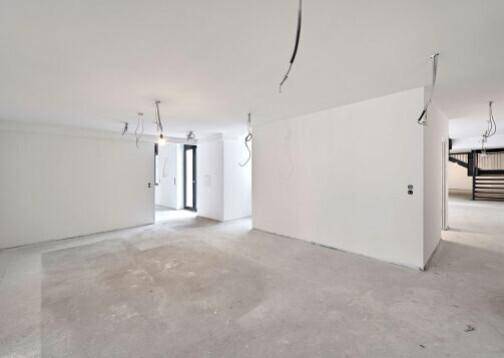 Heller, offener Gewerberaum mit weißen Wänden, Betonboden und sichtbaren Elektroinstallationen.
