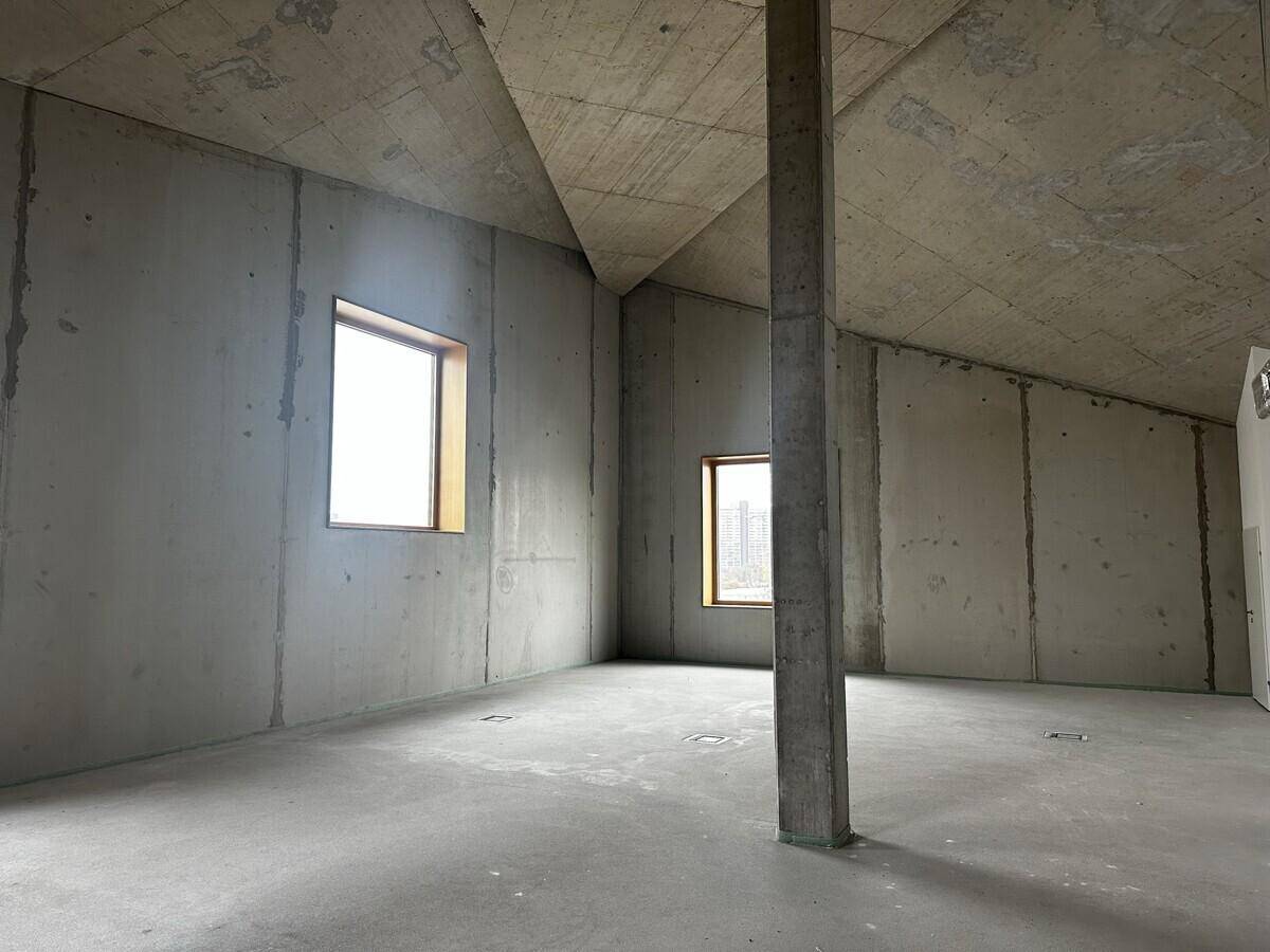 Heller Raum mit schrägen Betonwänden und -decken, ideal für ein Büro oder Atelier.
