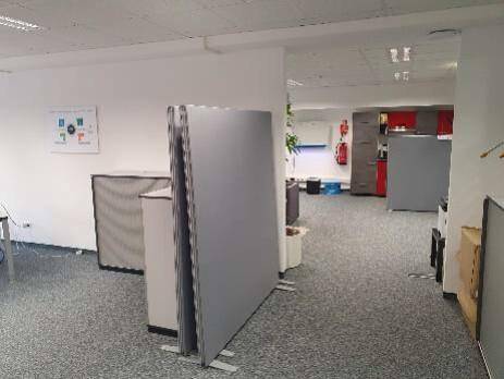 Offener Bürobereich mit modularen Trennwänden und Teppichboden, der in einen weiteren Arbeitsbereich führt.