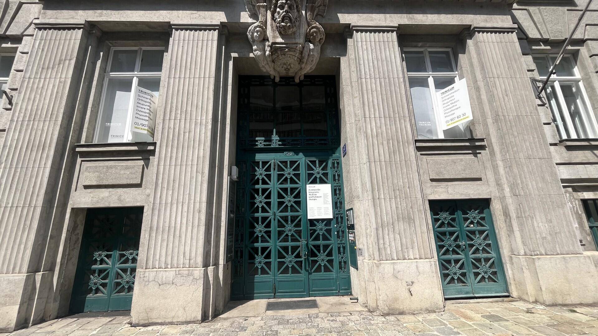 Detailansicht des Haupteingangs eines historischen Gebäudes mit verzierten grünen Türen und Säulen.