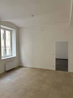 Geräumiger, leerer Raum mit hellem Boden und einem Fenster, das in einen weiteren Bereich blickt.